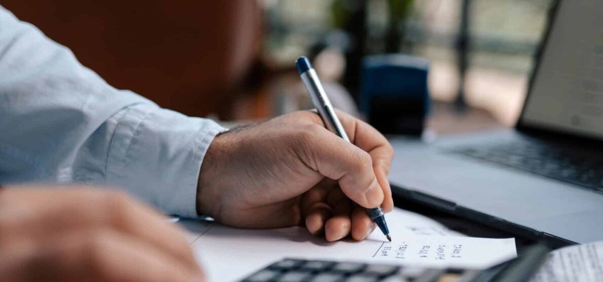 Free A person calculating finances with a calculator and pen on a desk indoors. Stock Photo