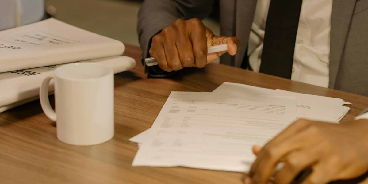 Free Close-up of a businessman holding and reviewing documents on a wooden desk. Stock Photo